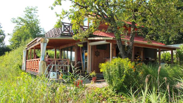 Ein Holzhaus mit rotem Dach und Veranda, umgeben von üppiger Vegetation.
