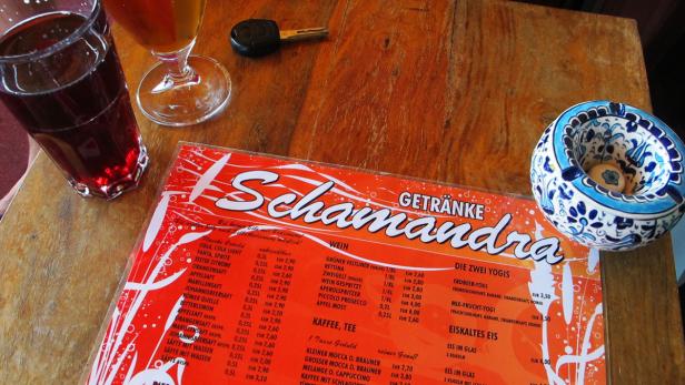 Ein Tisch mit Getränken, einer Speisekarte des „Schamandra“ und einem Aschenbecher.