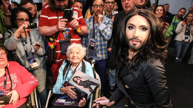 Conchita Wurst gibt einer älteren Dame im Rollstuhl ein Autogramm.