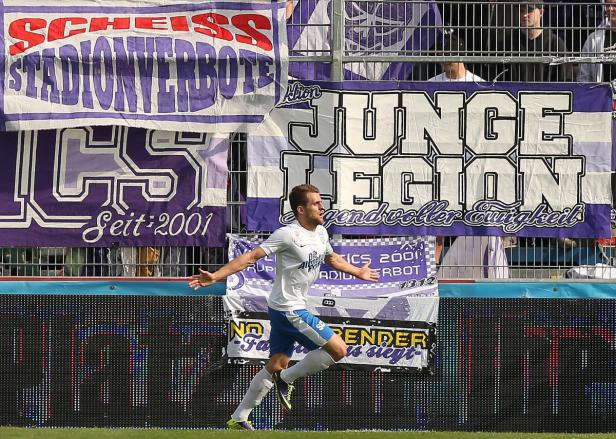 Ein Fußballspieler jubelt vor einer Tribüne mit Fanbannern.