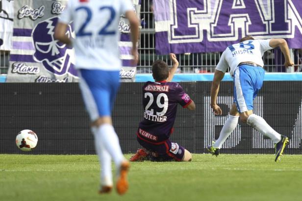 Ein Fußballspieler kniet auf dem Rasen, während andere Spieler im Hintergrund zu sehen sind.