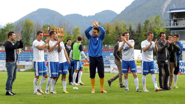 Eine Gruppe Fußballspieler und Fans applaudieren auf einem grünen Spielfeld.