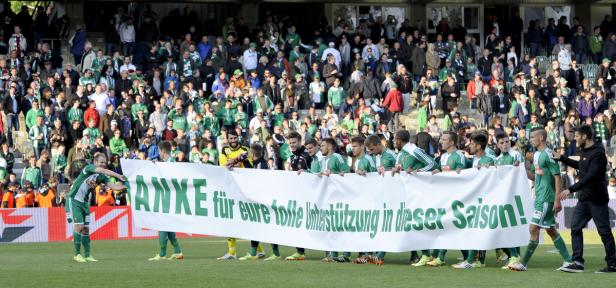 Eine Fußballmannschaft hält ein Banner mit der Aufschrift „Danke für eure tolle Unterstützung in dieser Saison!“ vor einer Zuschauermenge.