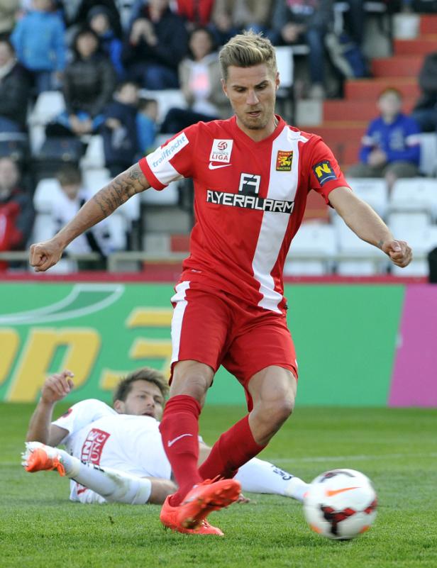 Ein Fußballspieler in Rot tritt gegen einen anderen Spieler auf dem Rasen.