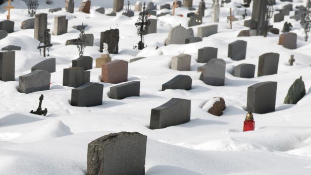 Ein verschneiter Friedhof mit Grabsteinen und einer roten Kerze.