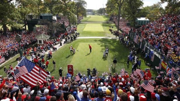 Ein Golfer beim Abschlag, umringt von einer großen Menschenmenge mit US-Flaggen.