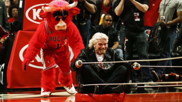 Richard Branson sitzt auf einem roten Kissen neben dem Maskottchen der Chicago Bulls.