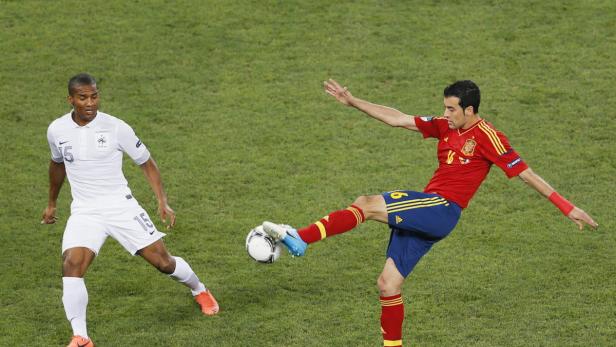 Ein spanischer Fußballspieler schießt den Ball, während ein französischer Spieler zusieht.