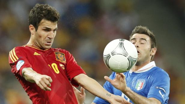 Zwei Fußballspieler, einer im roten spanischen Trikot, der andere im blauen italienischen Trikot, kämpfen um den Ball.