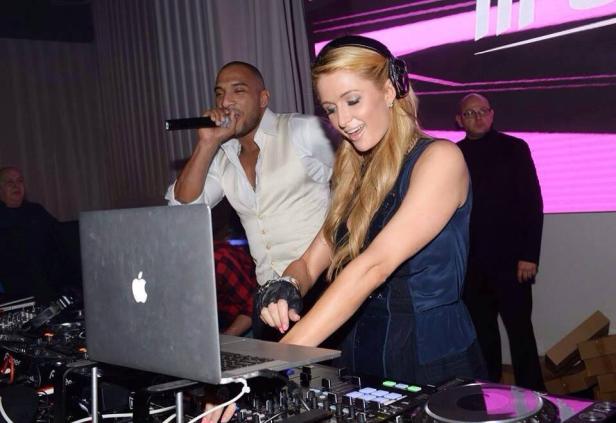 Paris Hilton legt als DJ auf, während ein Mann ins Mikrofon singt.