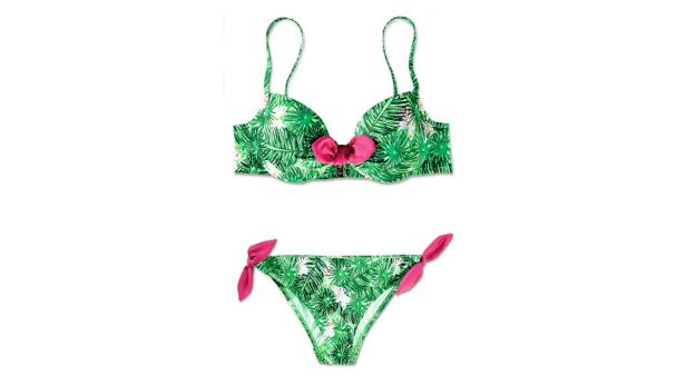 Ein grüner Bikini mit Palmenmuster und pinkfarbenen Schleifen liegt auf einem weißen Hintergrund.