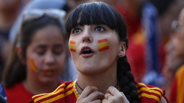 Eine junge Frau mit aufgemalten spanischen Flaggen auf den Wangen schaut aufmerksam zu.