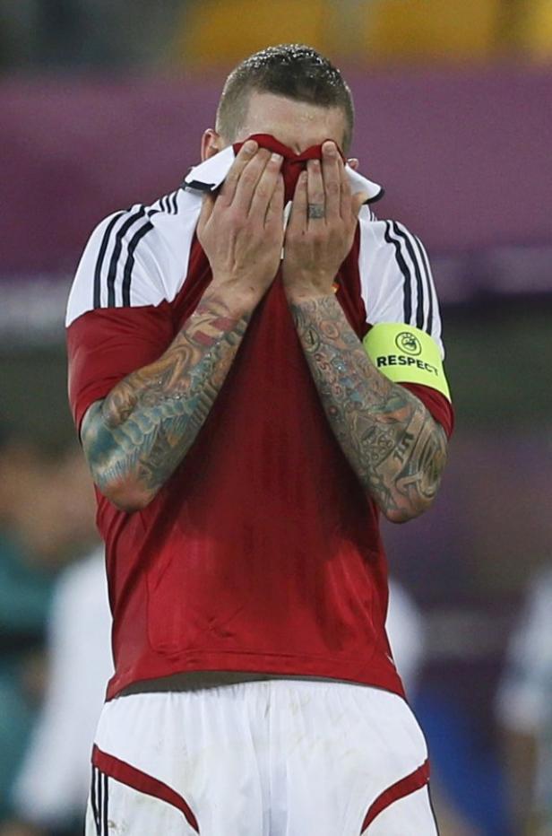 Ein Fußballspieler mit Tattoos verdeckt sein Gesicht mit seinem Trikot.