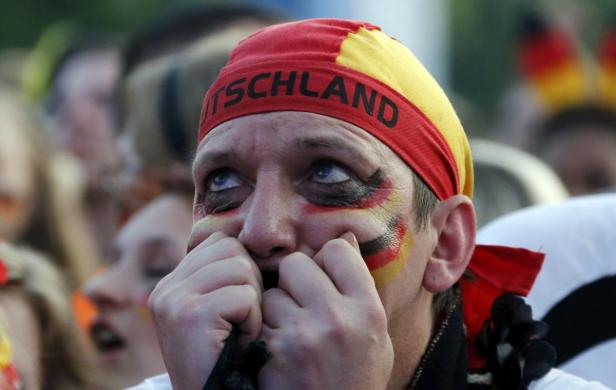Ein besorgter deutscher Fußballfan mit Deutschland-Schminke und Stirnband sieht aufgeregt nach oben.