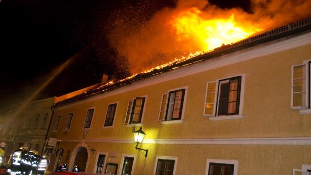 Ein gelbes Gebäude steht in Flammen, während Feuerwehrleute versuchen, das Feuer zu löschen.