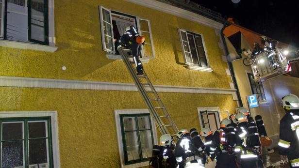 Feuerwehrmann steigt über eine Leiter in ein Fenster eines gelben Gebäudes.
