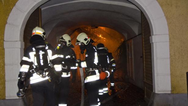 Mehrere Feuerwehrleute stehen vor einem brennenden Gebäude.
