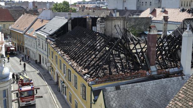 Ein Gebäude mit einem durch einen Brand zerstörten Dach und Feuerwehrfahrzeugen auf der Straße.