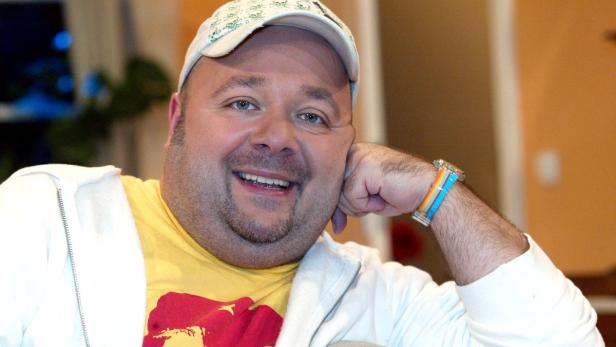 Ein lächelnder Mann mit Kappe und gelbem T-Shirt posiert für ein Foto.