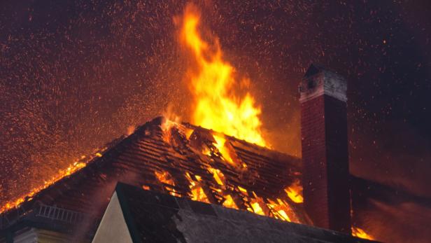 Ein Haus steht in Flammen, Funken fliegen in der dunklen Nacht.