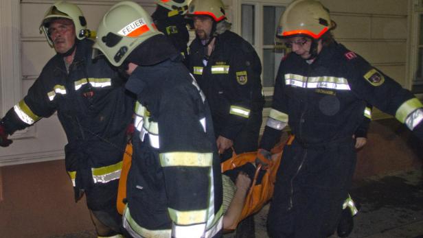 Mehrere Feuerwehrleute tragen eine Person auf einer Trage.