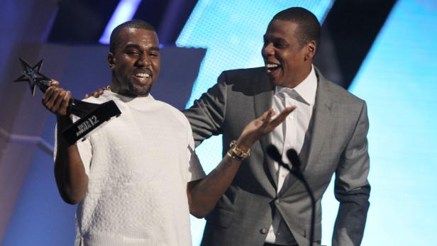 Kanye West hält eine Trophäe bei den BET Awards 2012, während Jay-Z daneben steht und lacht.