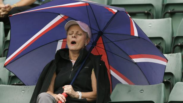 Eine Frau sitzt unter einem Regenschirm mit dem Union Jack Muster und gähnt.