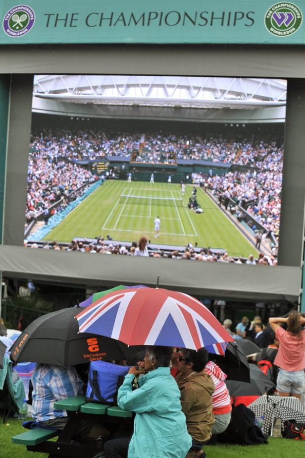 Zuschauer verfolgen ein Tennisspiel in Wimbledon auf einer Großbildleinwand.