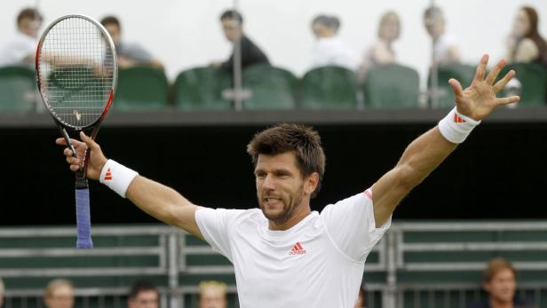 Ein Tennisspieler mit erhobenen Armen und Tennisschläger feiert einen Sieg.