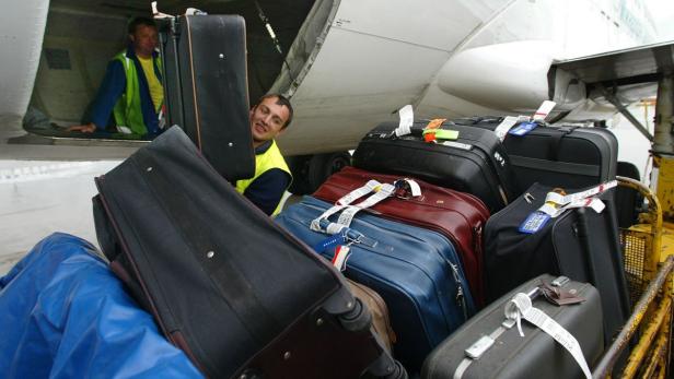 Gepäck wird in ein Flugzeug verladen, während zwei Arbeiter zusehen.