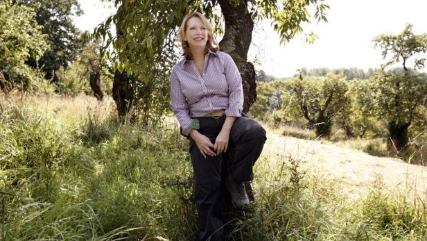 Eine Frau lehnt an einem Baum in einer grünen Landschaft.