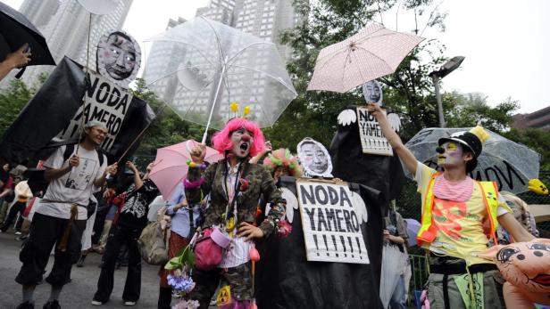 Eine Gruppe von Demonstranten, einige als Clowns verkleidet, hält Schilder und Regenschirme bei einer Kundgebung.