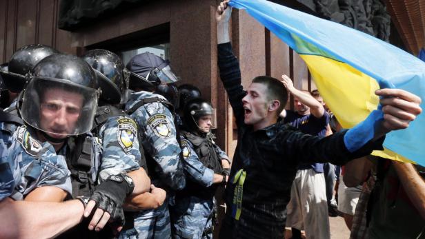 Ein Demonstrant schwenkt eine ukrainische Flagge vor einer Reihe von Polizisten.
