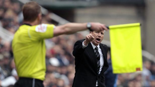 Ein Fußballtrainer gestikuliert neben einem Linienrichter mit erhobener gelber Fahne.