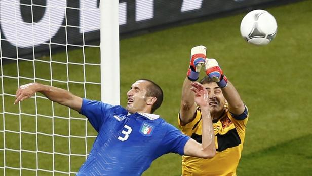 Ein Fußballspieler im blauen Trikot versucht, einen Ball vor dem Torwart abzuwehren.