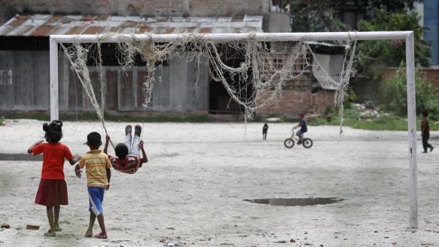 Kinder spielen mit einem kaputten Fußballtor auf einem staubigen Platz.