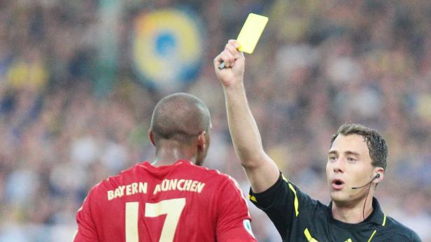Ein Schiedsrichter zeigt einem Bayern München Spieler die gelbe Karte.