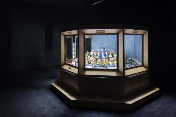 Ein beleuchteter Vitrinenschrank zeigt Spielzeugfiguren vor einem blauen Himmel-Hintergrund.