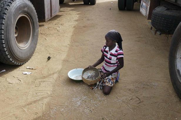 Ein Mädchen kniet auf dem Boden und reinigt Getreide mit einem Sieb.