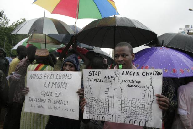 Eine Gruppe von Menschen demonstriert unter Regenschirmen mit Schildern in der Hand.