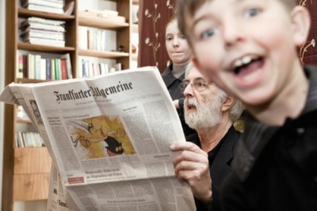 Scholz & Friends Berlin/F.A.Z/Dahinter steckt immer ein kluger Kopf/Michael Haneke/Making of (c: scholz & friends) Ein Mann liest die Frankfurter Allgemeine Zeitung, während ein Junge aufgeregt in die Kamera schaut.
