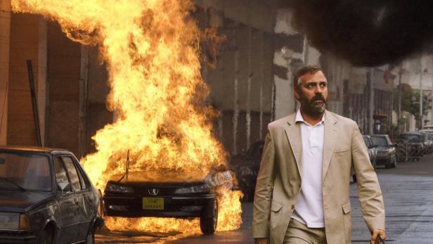 George Clooney geht vor einem brennenden Auto in Beirut entlang.