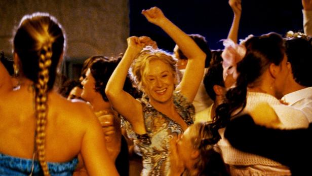 Meryl Streep tanzt ausgelassen auf einer Party, umgeben von anderen feiernden Menschen.