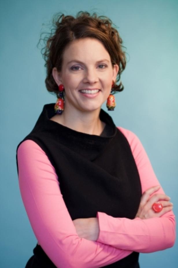 Sabine Hoffmann (c: werbeplanung.at/koekkoek) Eine lächelnde Frau mit verschränkten Armen, trägt Ohrringe in Form von Matroschkas.