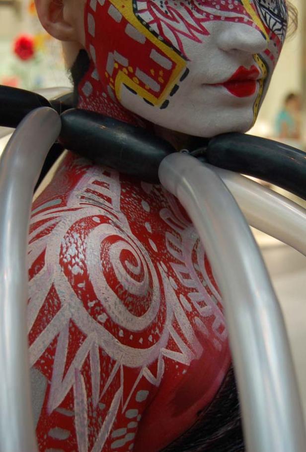 Eine Person mit aufwendiger Körper- und Gesichtsbemalung und Ballons um den Hals.