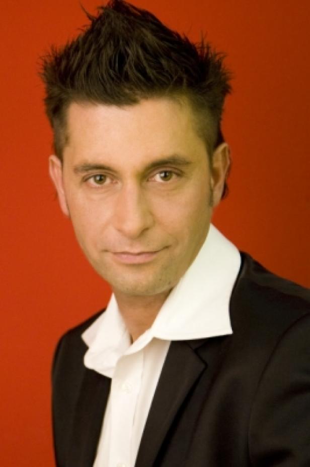 Christian Deutsch, deutschcom Ein Mann mit dunklem Haar und Anzug vor rotem Hintergrund.