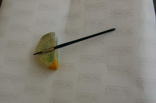 Ein Pinsel liegt auf einem bemalten Schwamm auf einem Blatt Papier.