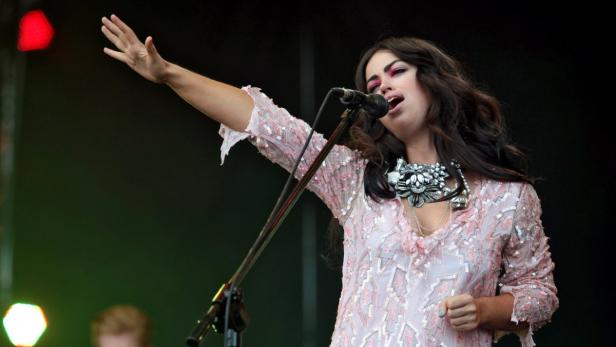 Eine Sängerin mit erhobenem Arm steht auf einer Bühne vor einem Mikrofon.