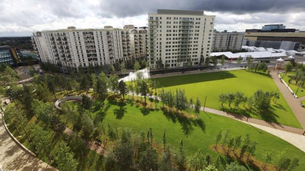 Blick auf einen Park mit Rasenflächen und modernen Wohngebäuden im Hintergrund.
