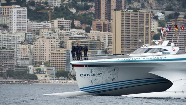 Die „Turanor PlanetSolar“ fährt vor der Küste von Monaco, mit vier Personen an Deck.
